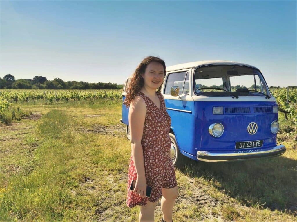 Combi VW vintage et femme souriante dans vignoble Jeune femme souriante près d'un combi VW vintage bleu et blanc dans un vignoble ensoleillé. Plaque DT-431-YE.