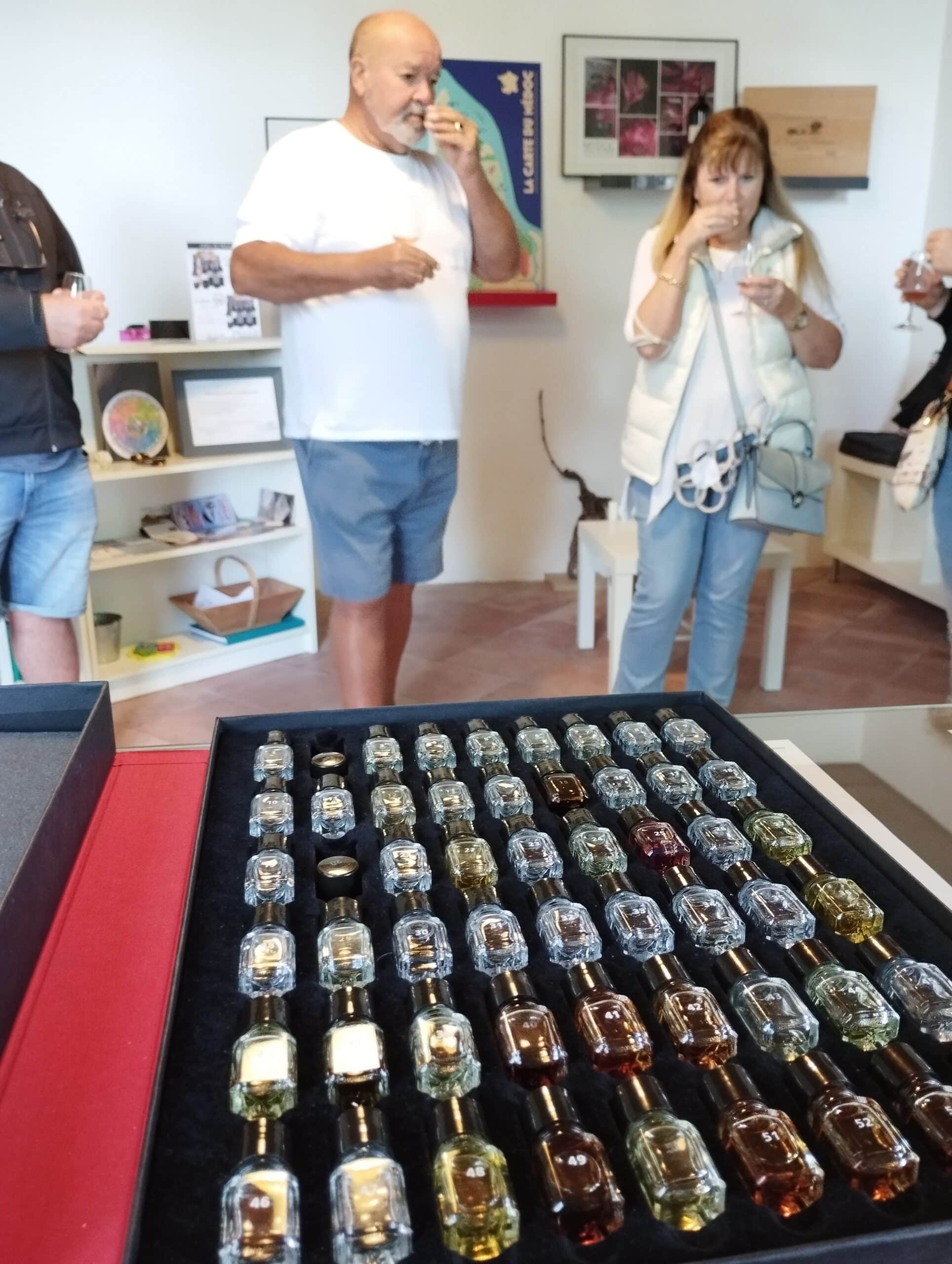 Personnes reniflant et dégustant des échantillons lors d'une session d'arômes, avec un plateau de fioles numérotées en premier plan. Carte du Médoc au mur.