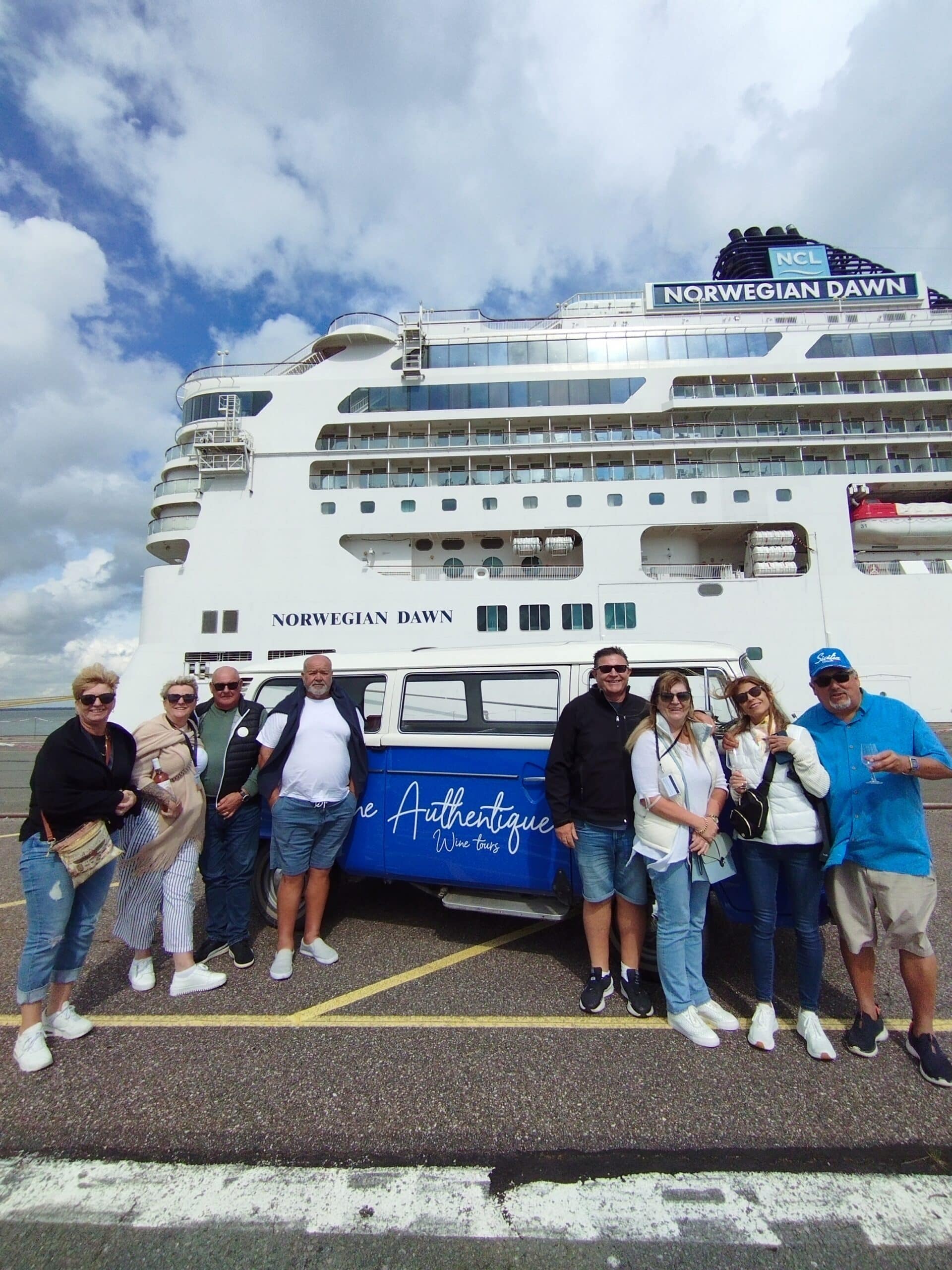 Groupe heureux devant le navire de croisière NORWEGIAN DAWN et un van bleu "The Authentique Wine tours" au port, certains tenant des verres de vin.